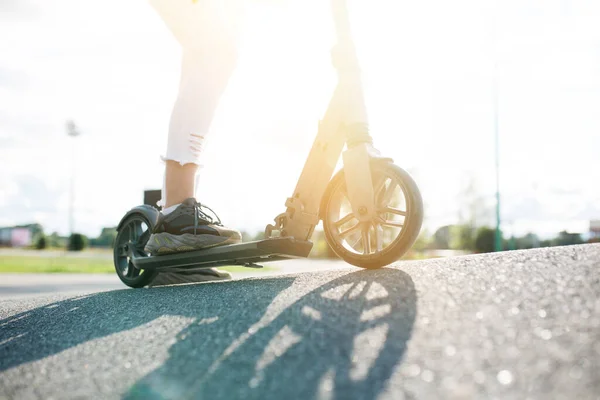 Primer plano de la parte inferior de un scooter y las piernas de una chica que está montando por la calle en vehículos adquiridos en un día soleado — Foto de Stock