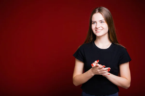 Uma menina bonita com cabelos longos ri e dobrou os braços na frente de si mesma contra um fundo vermelho. Conceito de retrato emocional — Fotografia de Stock