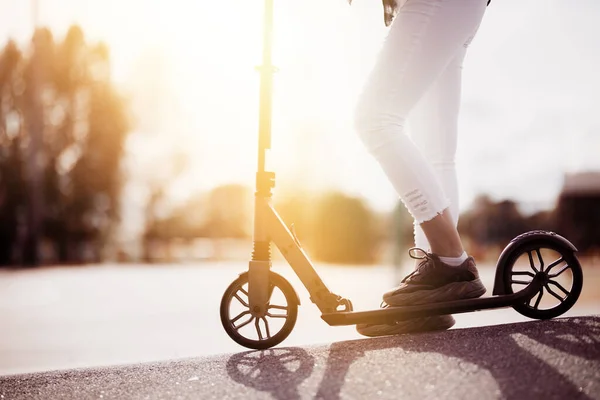 Ένα κοντινό πλάνο του πυθμένα του σκούτερ και τα πόδια ενός κοριτσιού που βόλτες κάτω από το δρόμο για αγορασμένη μεταφορά σε μια ηλιόλουστη μέρα — Φωτογραφία Αρχείου