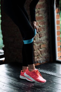 Çatı katında kas eğitimi için mavi spor lastiği taktıkları pembe spor ayakkabılı bir kızın bacaklarının yakın çekimi.
