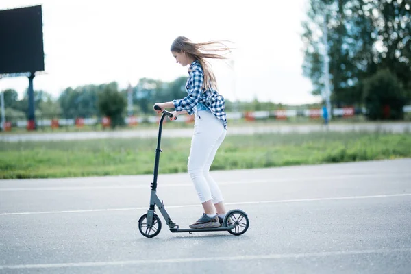 Una chica monta un scooter a lo largo de una zona pavimentada y lisa del parque. Actividades deportivas durante la caminata por el hambre . —  Fotos de Stock