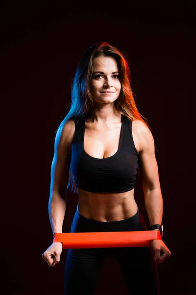 Menina com pressão aumentada no topo do esporte está envolvida com uma banda de esportes de borracha para o exercício em um fundo preto . — Fotografia de Stock