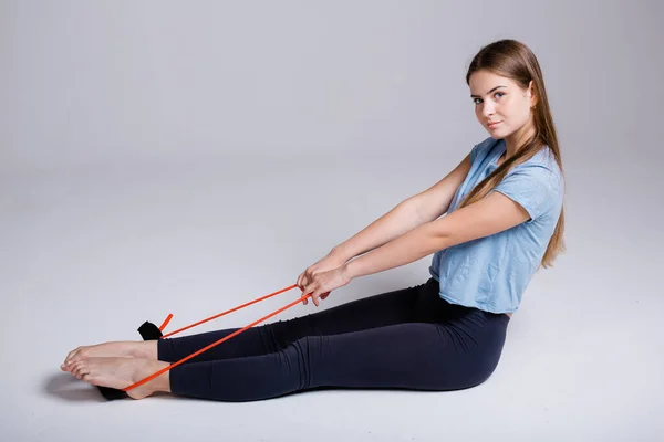 Дівчина робить ранкові вправи з помаранчевою еластичною стрічкою для спортивних тренувань. Підтримка м'язів і тіла в тоні . — стокове фото