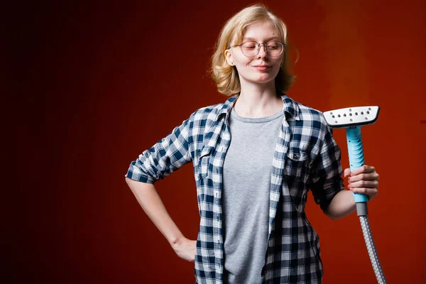 Una chica rubia en gafas toma una mano en la cintura y mira a un nuevo vapor profesional sobre un fondo rojo —  Fotos de Stock