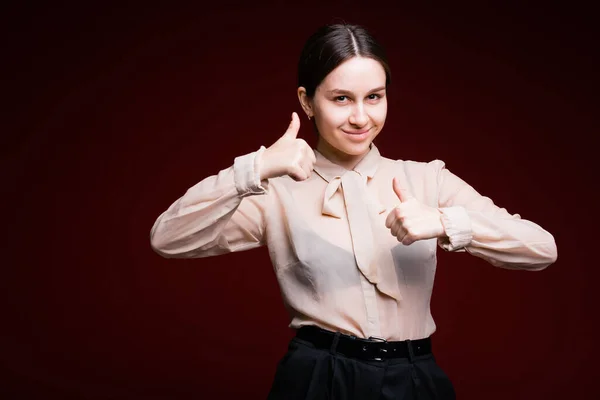 Πορτρέτο μιας επαγγελματικής κοπέλας που χαμογελά ελαφρά και δείχνει τους αντίχειρες της σε μια παρόμοια πινακίδα σε ένα κόκκινο φόντο — Φωτογραφία Αρχείου