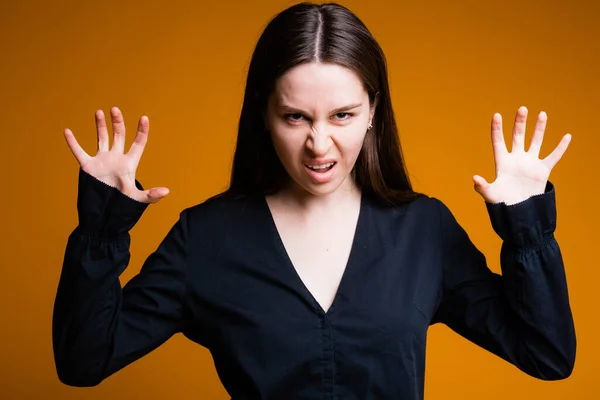 Uma garota assustadora em uma camisa preta com as mãos e rosto sorri e mostra suas garras para quebrar com raiva em um fundo amarelo — Fotografia de Stock