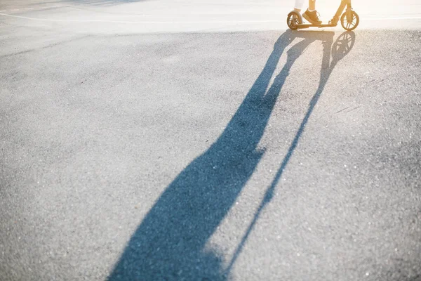 Foto de un hombre montando un scooter y una larga sombra cayendo sobre el asfalto exterior. Concepto de artículos deportivos —  Fotos de Stock