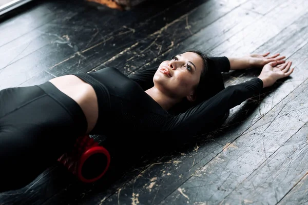 Вгорі вимальовується дівчина з Азії, яка лежить у чорній спортивній формі на підлозі і вимальовує пухнасті м "язи з пінопластом. — стокове фото