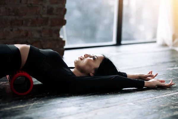 Bagian atas tubuh seorang gadis memijat fasia otot lumbar peregangan lengannya sepanjang lantai kayu di gym — Stok Foto