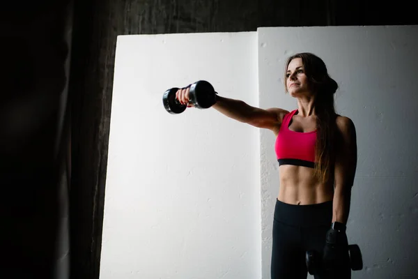 Retrato de uma jovem pugilista com cabelos longos e uma imprensa nua esticando o braço para a frente com halteres pesados para treinar os músculos dos braços — Fotografia de Stock
