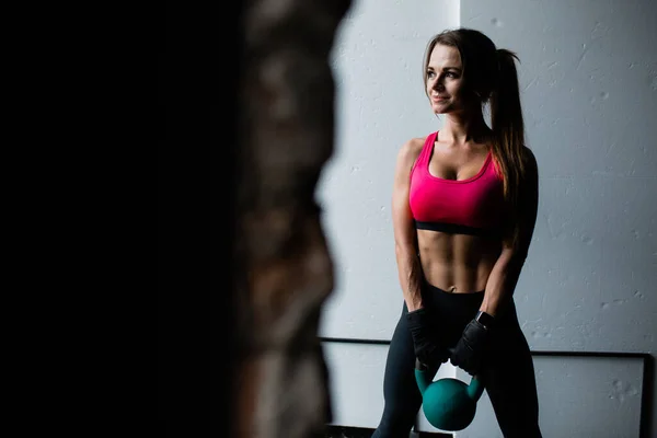 Retrato de una joven levantadora de pesas en un top rosa y polainas negras que entrena levantando una pesada kettlebell sobre un fondo blanco —  Fotos de Stock