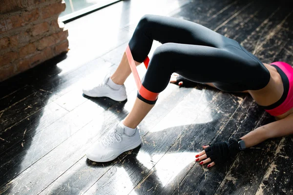 Uma visão aérea das pernas de uma jovem mulher que estava na ponte e colocou um expansor de borracha elástica em suas pernas para treinar músculos das pernas . — Fotografia de Stock