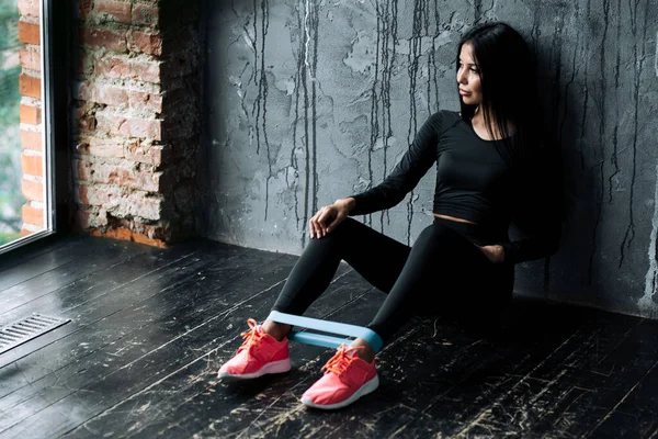 Молода жінка сидить на підлозі біля стіни з еластичним гумовим екстрактором для тренування м'язів ніг — стокове фото