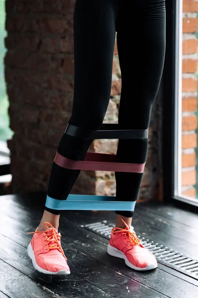 Primer plano de las piernas femeninas en zapatillas de deporte de color rosa y polainas negras con tres expansores elásticos de goma para la demostración de artículos deportivos —  Fotos de Stock