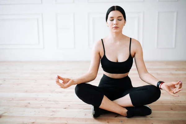 Jonge vrouw in sportkleding zit op de vloer en mediteert met haar ogen dicht na yoga. — Stockfoto
