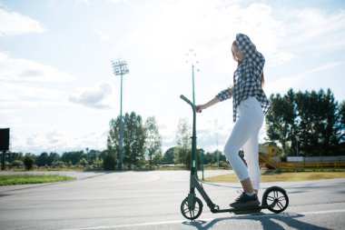 Parlak bir fotoğraf, genç bir kadın bir şehir meydanının ortasında mobiletiyle durmuş. Kentsel bir ortamda spor yaparken dinlenin.