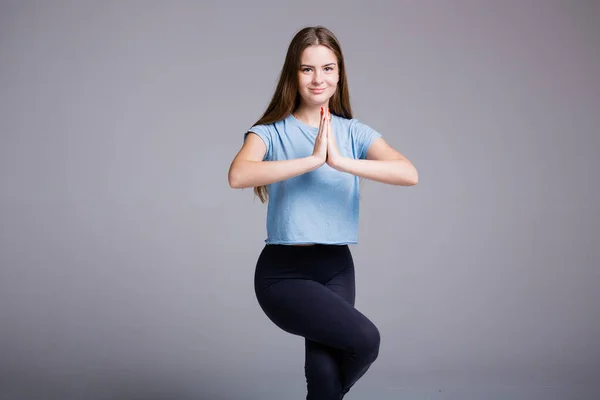 Молода жінка в одязі йоги стоїть на одній нозі і медитує зі своїми долонями разом перед нею. Спортивна жінка з довгим волоссям . — стокове фото