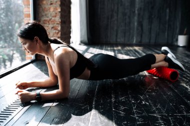 Tavan arasındaki bacak kaslarına masaj yapmak için ellerini yere koyan genç bir kadının yan görüntüsü.