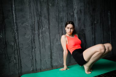 Profesyonel bir yoga eğitmeni, kollarına ve bacaklarına yaslanıp köpük bir mindere otururken kaslarını esnetmenin temel kurallarını gösterir..