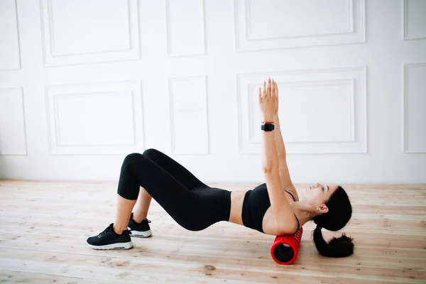 Asiatiska kvinnliga idrottskvinna gör en övning för att stärka musklerna i ryggen och höfterna med hjälp av massagerulle för fascia. — Stockfoto