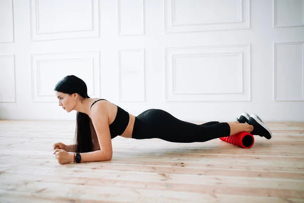 Asiatisk kvinna atlet i en svart topp och sport leggings utför en planka övning med hjälp av en massagerulle under yoga. — Stockfoto