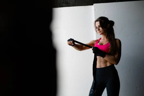 Retrato de una entrenadora de pilates con el pelo largo en una parte superior rosa que ata sus manos con un vendaje deportivo negro antes de levantar pesadas mancuernas sobre fondo blanco —  Fotos de Stock