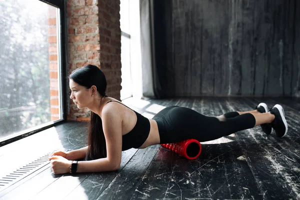 Pilatestränaren står i en planka och arbetar framtill på låret med en massagerulle — Stockfoto