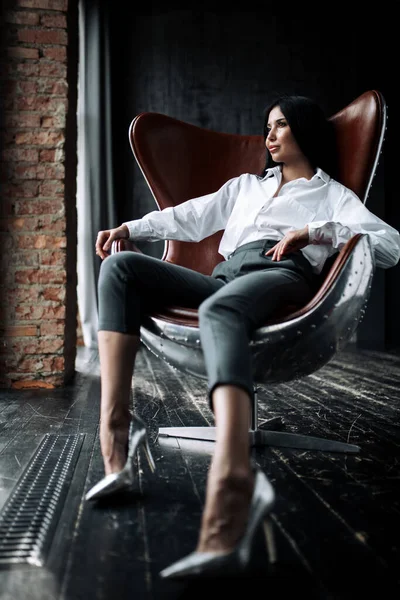 Жіночий офісний працівник відпочиває у кріслі. Азійська комерсантка сидить у білій сорочці та сірих штанях на горищі. — стокове фото