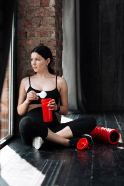 Kız sporcu yerde oturur ve sporu kırmızı bir içeceğe koyar.