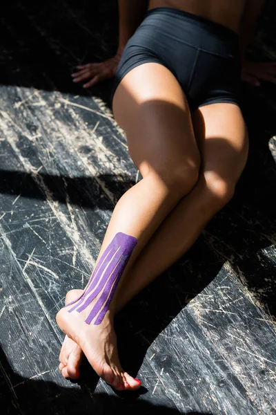 Primer plano de las piernas femeninas. Una chica se sienta en el suelo con una cinta de kinesioterapia en la parte inferior de la pierna — Foto de Stock