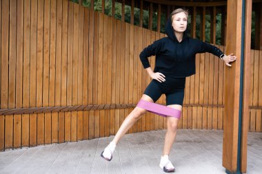 Spor yapan bir kız elastik bantla egzersiz yapıyor. Açık hava egzersizi.