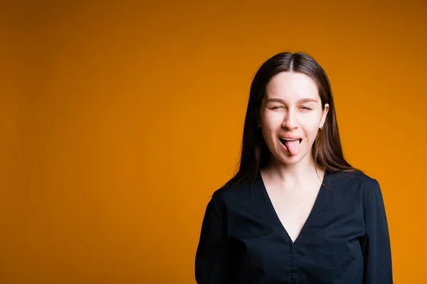 Dziewczyna pokazuje swój język. Stojak na pomarańczowym tle — Zdjęcie stockowe