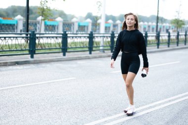 Siyah spor üniformalı bir kız elinde sallayıcıyla sokakta dikiliyor.