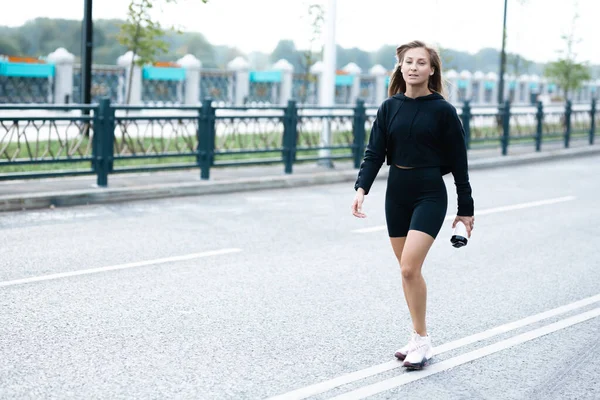 검은 색 스포츠 유니폼을 입은 한 소녀가 손에 샤커를 들고 거리에 서 있다 — 스톡 사진