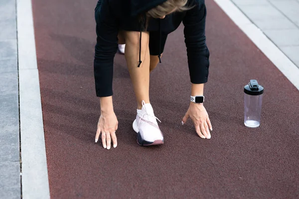 Una chica se encuentra en una posición de inicio bajo en una cinta de correr — Foto de Stock