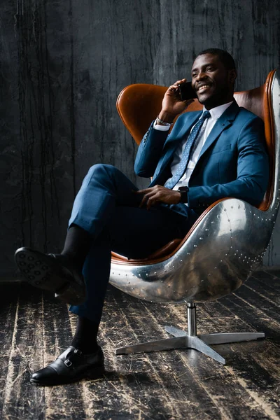Een zwarte man in een blauw pak zit in een vliegeniersstoel, praat aan de telefoon en lacht. — Stockfoto