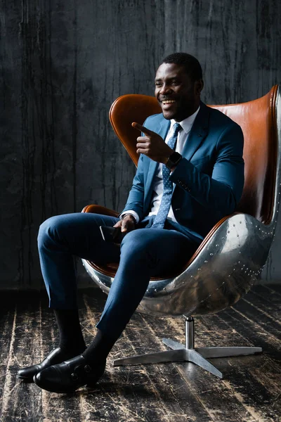 Hombre afroamericano sentado en una silla de oficina y mostrando su dedo índice —  Fotos de Stock