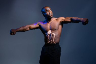 Vücudunda Kinesio bantları olan siyah erkek sporcu gri bir arka planda duruyor.