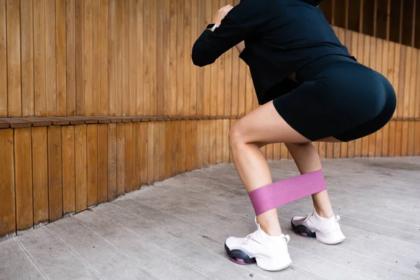 Flicka i svart sportuniform som knäböjer med resårband för träning — Stockfoto