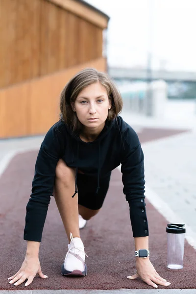 Atleta menina fica em uma posição de partida baixa em uma esteira e se prepara para uma corrida — Fotografia de Stock