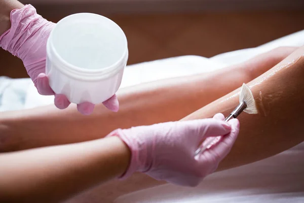 Фото рук в розовых медицинских перчатках, наносящих охлаждающий косметический гель с кистью. Подготовка кожи к процедуре — стоковое фото