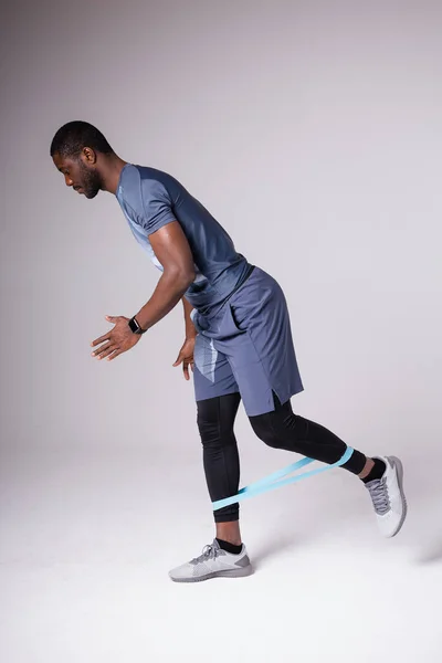 Αρσενικό Αφρικής Αμερικανός γυμναστής εκτελεί μια άσκηση με ένα ελαστικό ιμάντα για προπονήσεις — Φωτογραφία Αρχείου