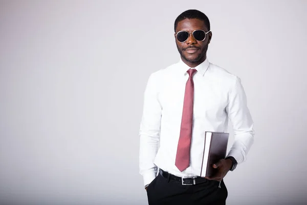 An African American man in a white shirt and tie stands on a white background. A man in sunglasses and a folder for documents in his hands — Stock Photo, Image