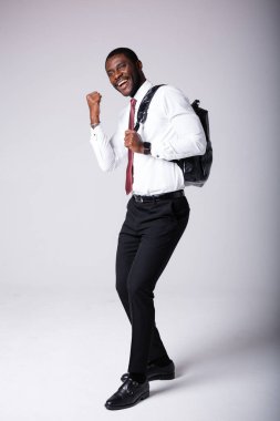 Omzunda siyah bir sırt çantası olan Afrikalı Amerikalı bir üniversite öğrencisi seviniyor. Beyaz bir arkaplanda durur