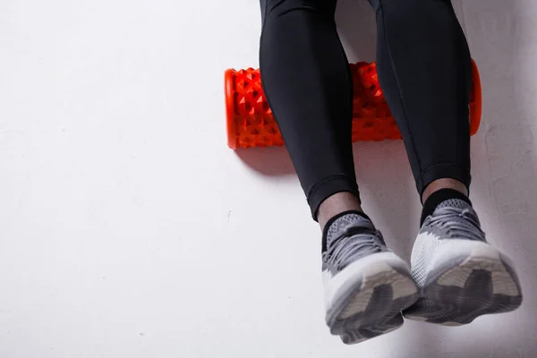 Un hombre resuelve la fascia de los músculos de la pantorrilla con un rollo de masaje de entrenamiento rojo. Piernas de cerca — Foto de Stock