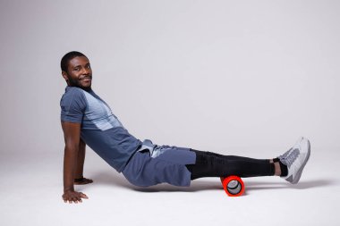 Erkek sporcu, kırmızı pilates masajı rulosu kullanarak baldır kaslarını çalıştırıyor.