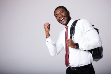 Omzunda siyah bir sırt çantası olan Afrikalı Amerikalı bir üniversite öğrencisi seviniyor. Beyaz bir arkaplanda durur