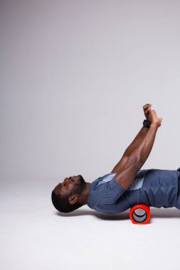 Siyah adam, beyaz arka planda masaj rulosuyla egzersiz gösteriyor.