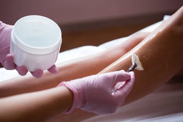 Фото рук в розовых медицинских перчатках, наносящих охлаждающий косметический гель с кистью. Подготовка кожи к процедуре — стоковое фото