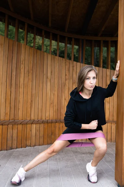 Entraîneur de fitness fille se jette sur le côté avec expanseur élastique pour les séances d'entraînement — Photo